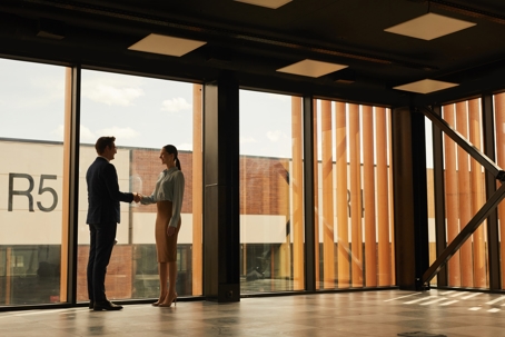 Real estate agent shaking hands with client while standing in empty office building