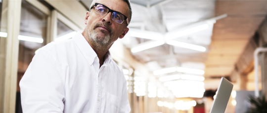 Businessman looking into the distance as if contemplating his options with a notebook and laptop on the table in front of him.
