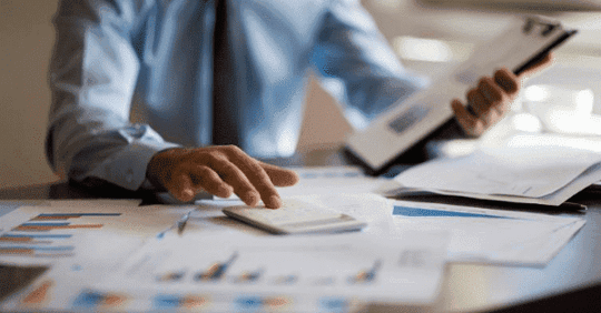 Business person looking at documents and using a calculator.