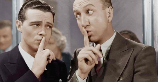 Vintage photo of two businessmen with their fingers to their lips indicating discretion.