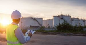 Engineer writing on paper clipped to a clipboard in front of the oil tank.