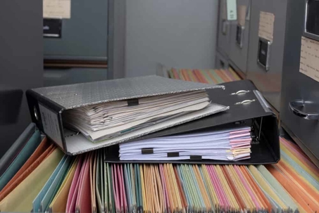 Two binders stacked on top of open file drawer of a metal filing cabinet.