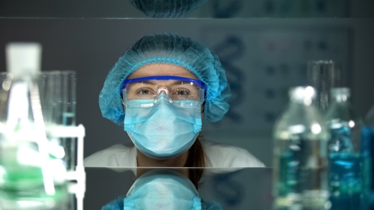 Laboratory worker in protective eyeglasses and uniform looking at camera.