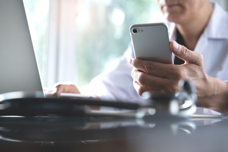 Male doctor talking to a telemedicine patient via cell phone in front of a laptop.