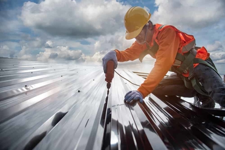 Worker with hand drill installing a metal roof.