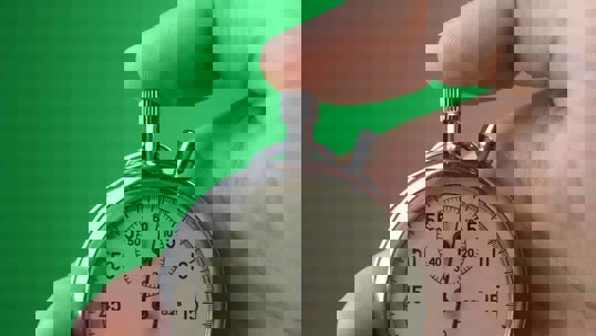 Close-up of male hand holding analogue stopwatch on green background.