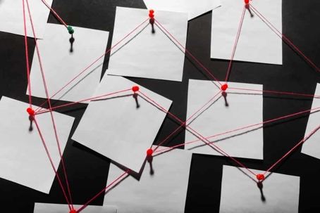 Photo of a black evidence board with blank paper linked by red thread.