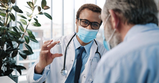 Close up of African American male doctor in medical mask talking with a senior patient.