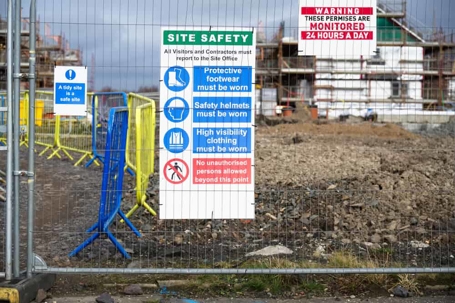 Sign at an outdoor job site with safety and hazard warnings and a reminder to employees to check in for safety briefing before entering the site.