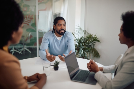 African American man communicating with two businesswomen in an office setting.