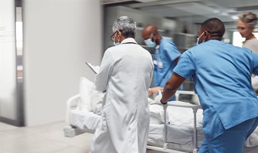 Busy healthcare professionals, including a doctor in a white lab coat and two nurses in scrubs, rush a patient to surgery.