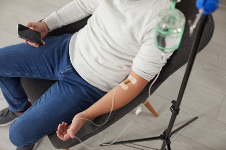 man receiving iv hydration treatment while looking at his cell phone.