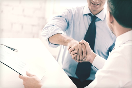 Two businessmen shake hands over a table.