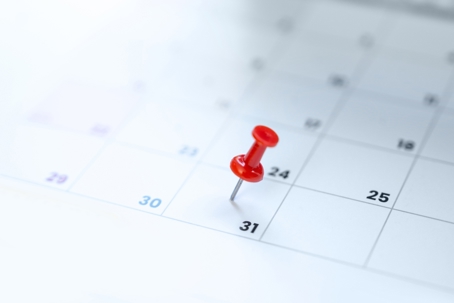 Red push pin on the 31st day of the month on a paper calendar.