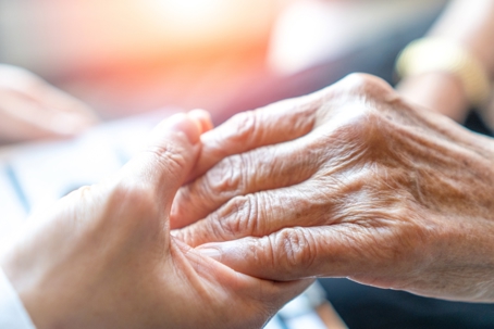 Caregiver holding elderly person's hand in hospice care
