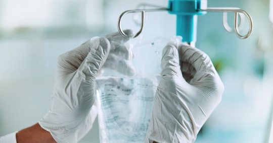 Close-up of healthcare professional's gloved hands hanging an IV bag on a stand.