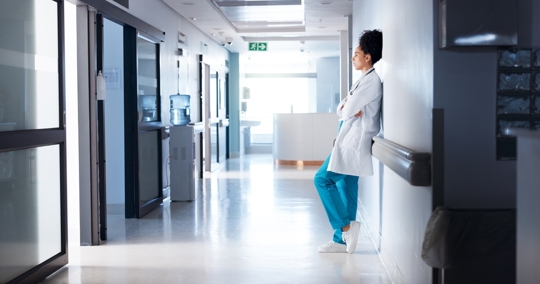 Overworked physician, arms crossed, in hospital hallway.