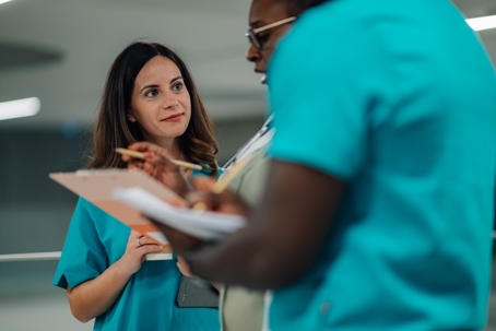 Nurses and doctors collaborating, discussing patient information on a clipboard.