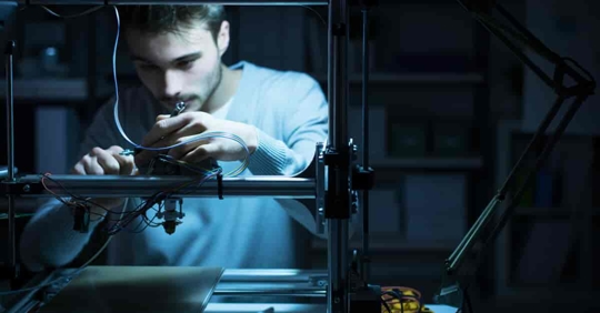 Young engineer working at night in the lab, adjusting a 3D printer's settings.