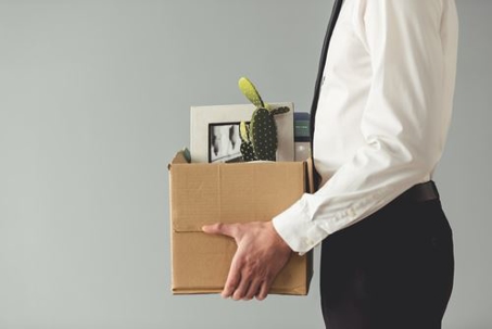 Side profile of a white male in business attire holding a box of personal office items.