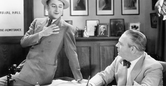 Vintage photograph of a businessman sitting on his boss' desk looking smug.