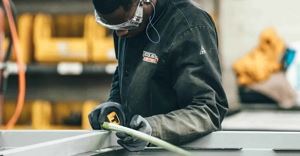 A worker in a manufacturing facility wearing safety glasses and coveralls measuring materials.