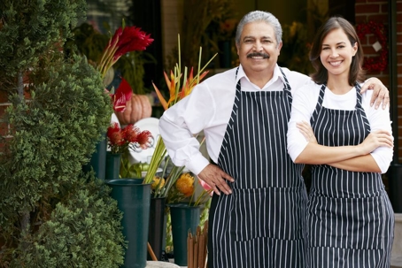 A father and daughter stand smiling in front of a family-owned florist business.
