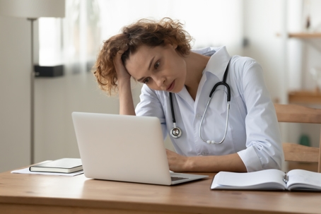 Stressed young female doctor looking at laptop