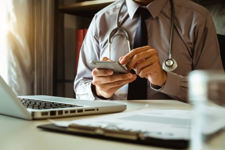 Close-up of a physician at his desk typing on a smart phone.