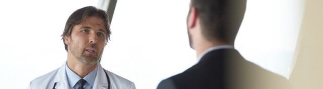  A male doctor in a white medical coat is approached by an OIG investigator in a hospital hallway regarding a potential False Claims Act violation