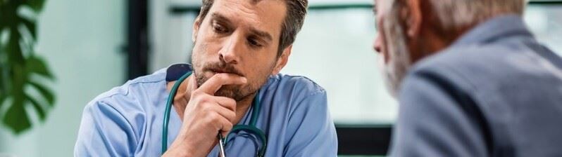 An older physician in a suit reviews a non-solicitation agreement on a laptop with a younger physician dressed in blue scrubs.