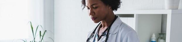 A concerned female physician in a white medical coat reads a notification that her medical practice is the target of a healthcare fraud investigation.