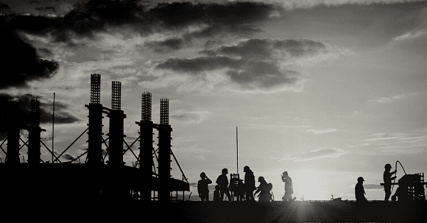 Black and white photograph of a construction crew working on a building profiled against the setting sun.